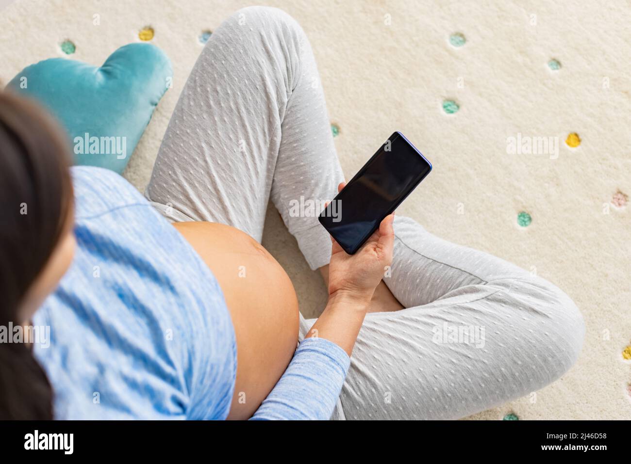 Pregnant woman using phone app for online social media or prenatal class. Top view of pregnancy bump at home Stock Photo