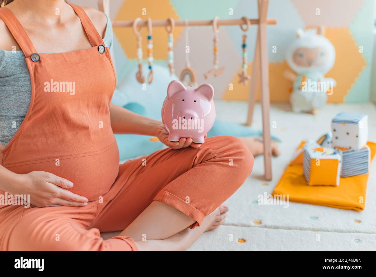 Pregnancy family planning budget. Cost of having a child. Pregnant woman holding piggy bank shopping newborn toys and nursery decor with savings Stock Photo