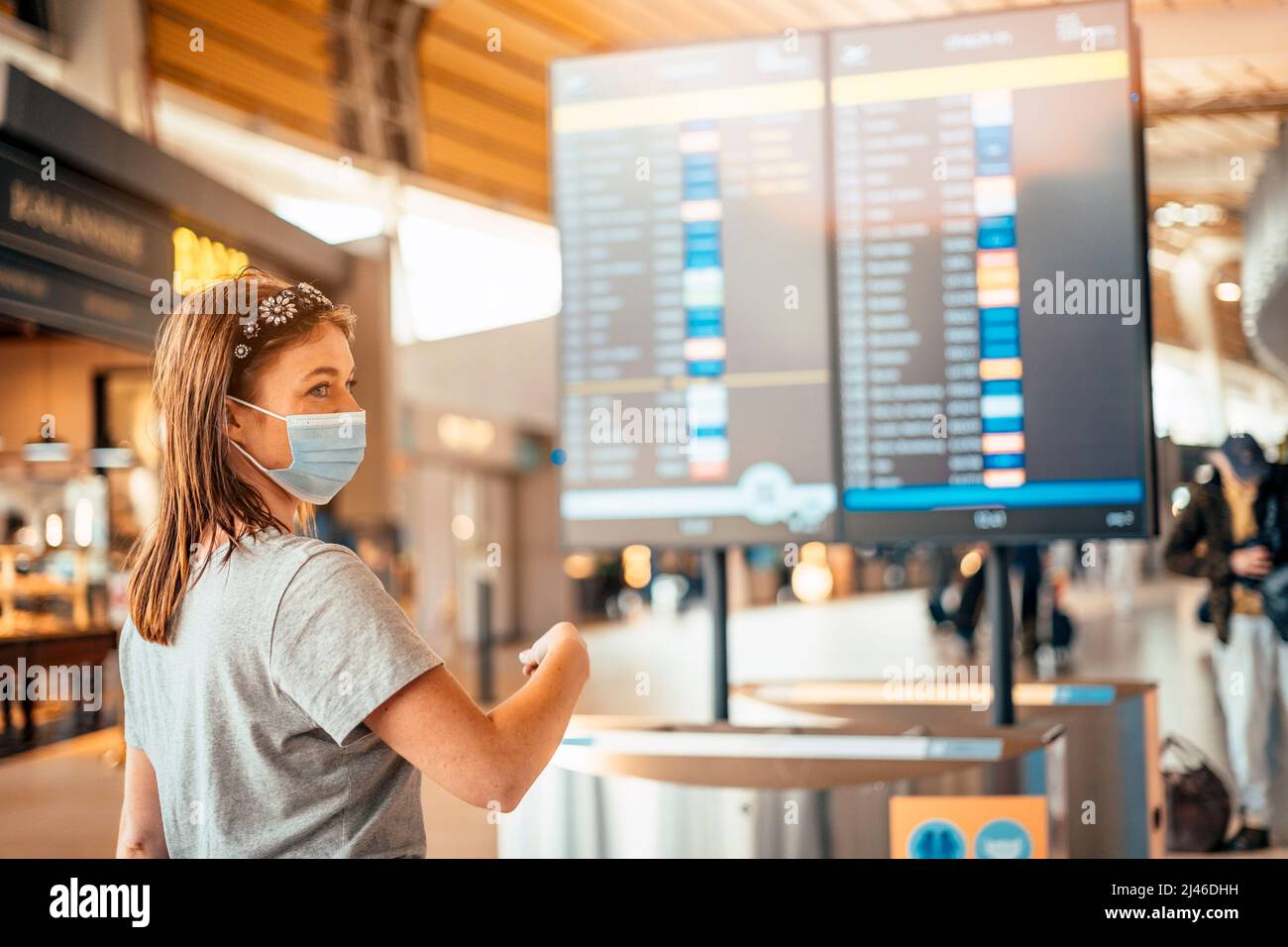 A young woman wearing mask by information board with timetable at the airport Stock Photo