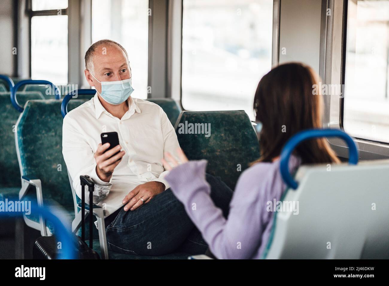 A couple of friends wearing mask and nicely talking while traveling by train Stock Photo