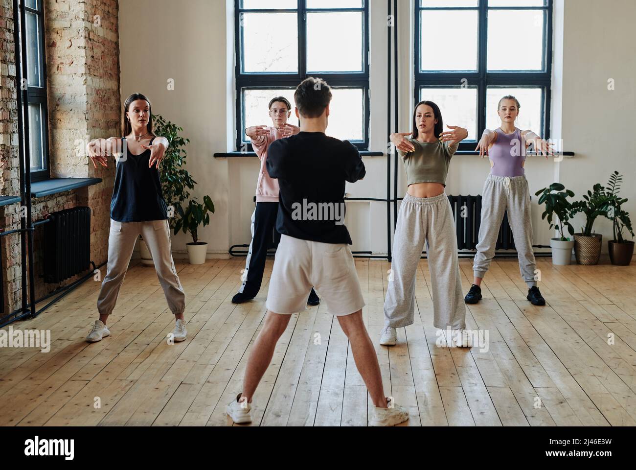Group of contemporary teenage girls and guy looking at dance instructor during repetition of vogue dancing in spacious studio Stock Photo