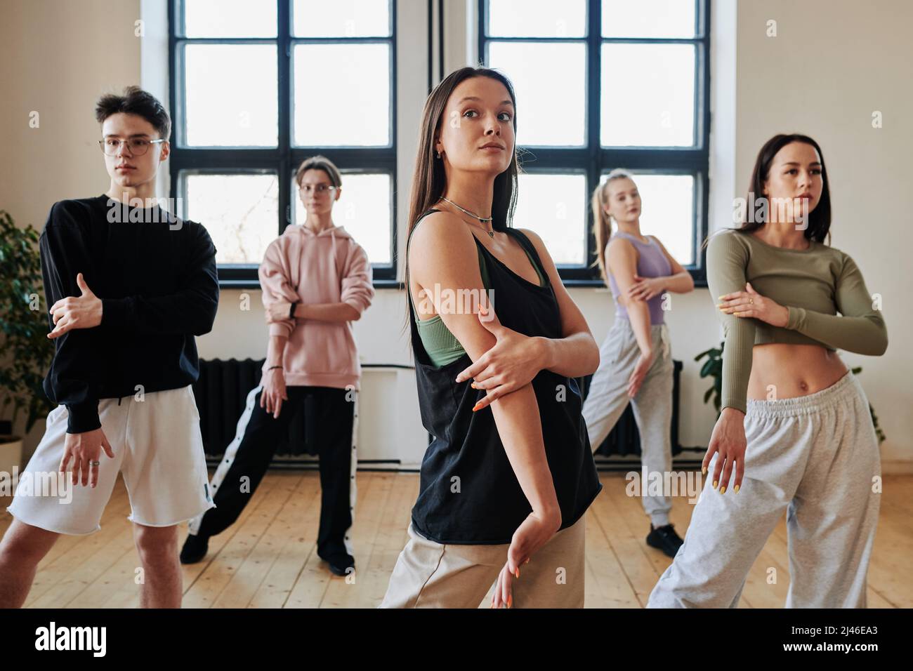 Group of contemporary teens in pants and tanktops repeating after dance instructor while learning new movements of vogue dancing Stock Photo