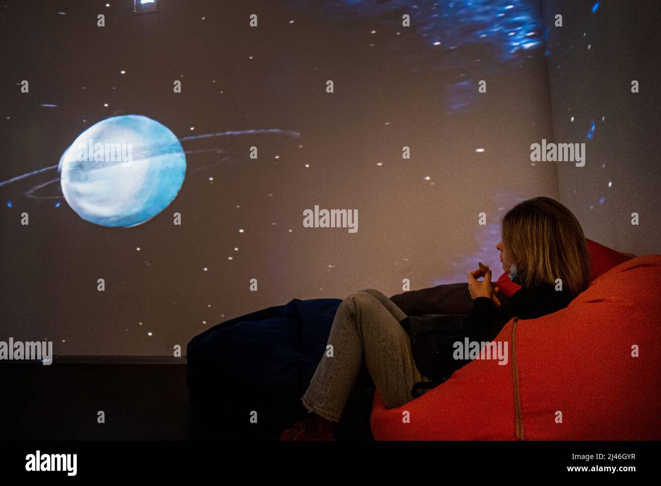 The girl faces the projection of the planet Saturn on the wall. Stock Photo