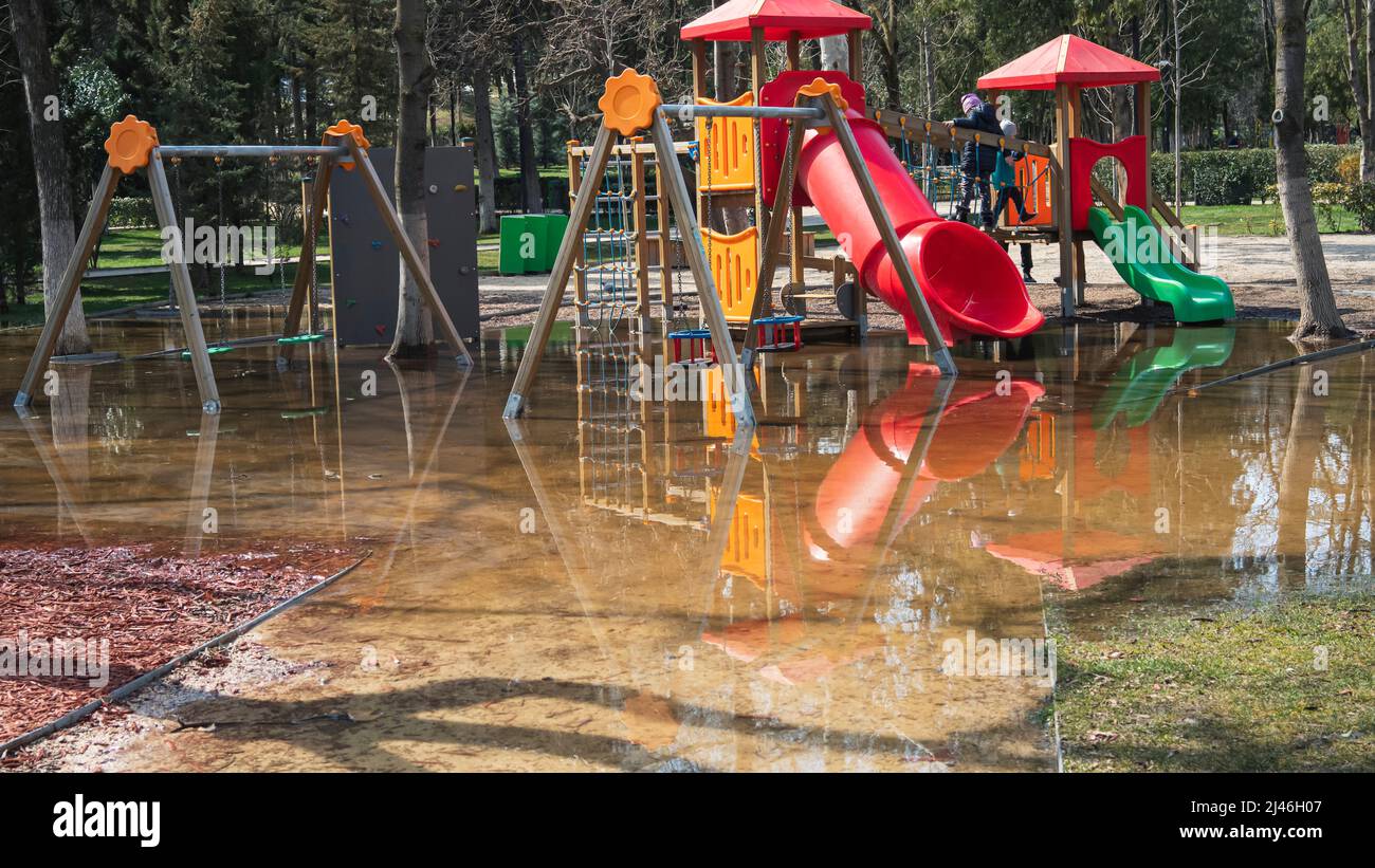 Children's playground in a public park in the city. The swing and pipes are in a puddle. Impossible to play Stock Photo