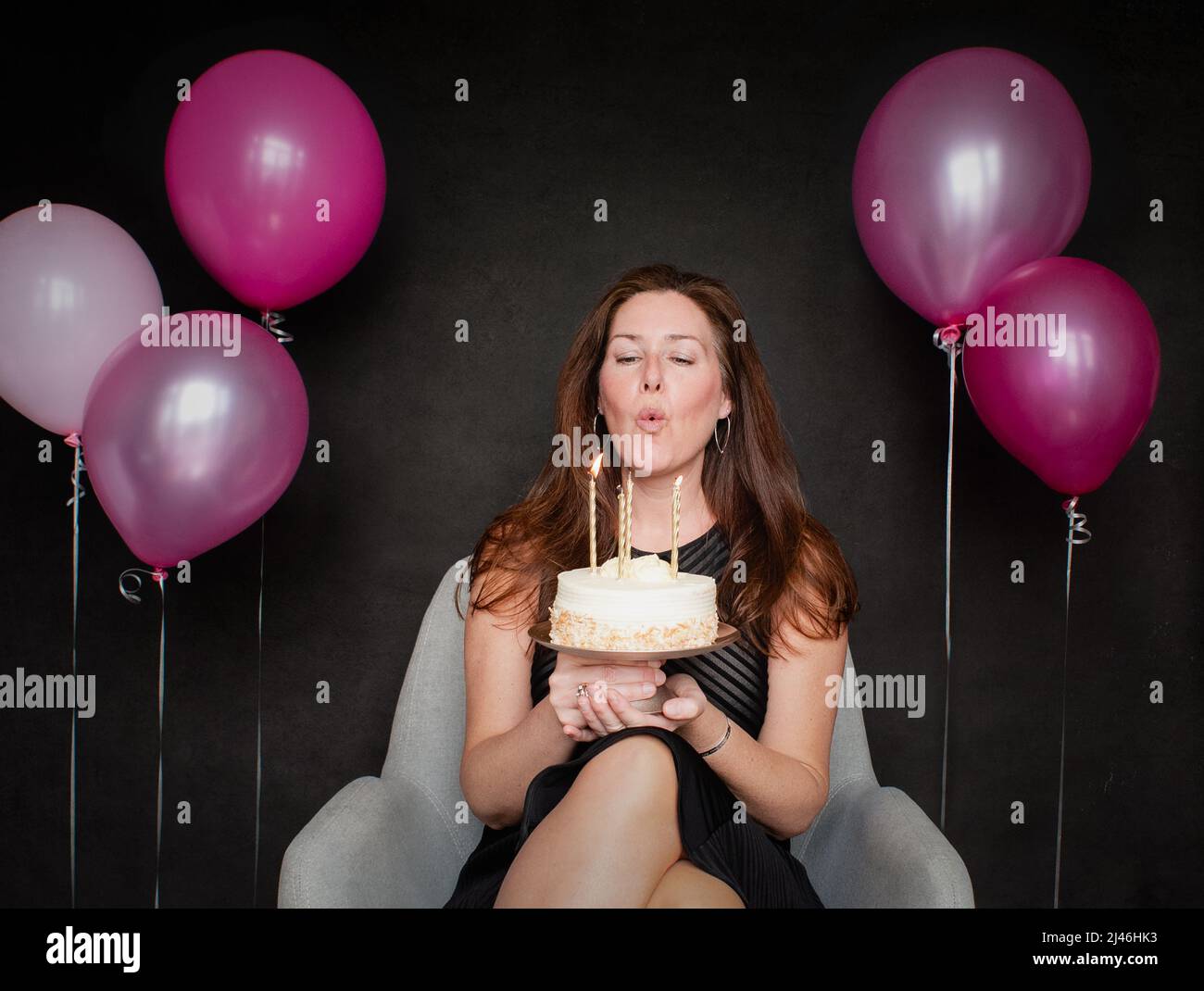 Pretty woman blowing candles out on birthday cake with balloons. Stock Photo