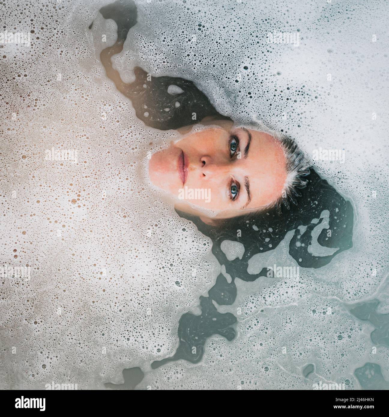 Overhead of woman's face in a bubble bath with head submerged Stock