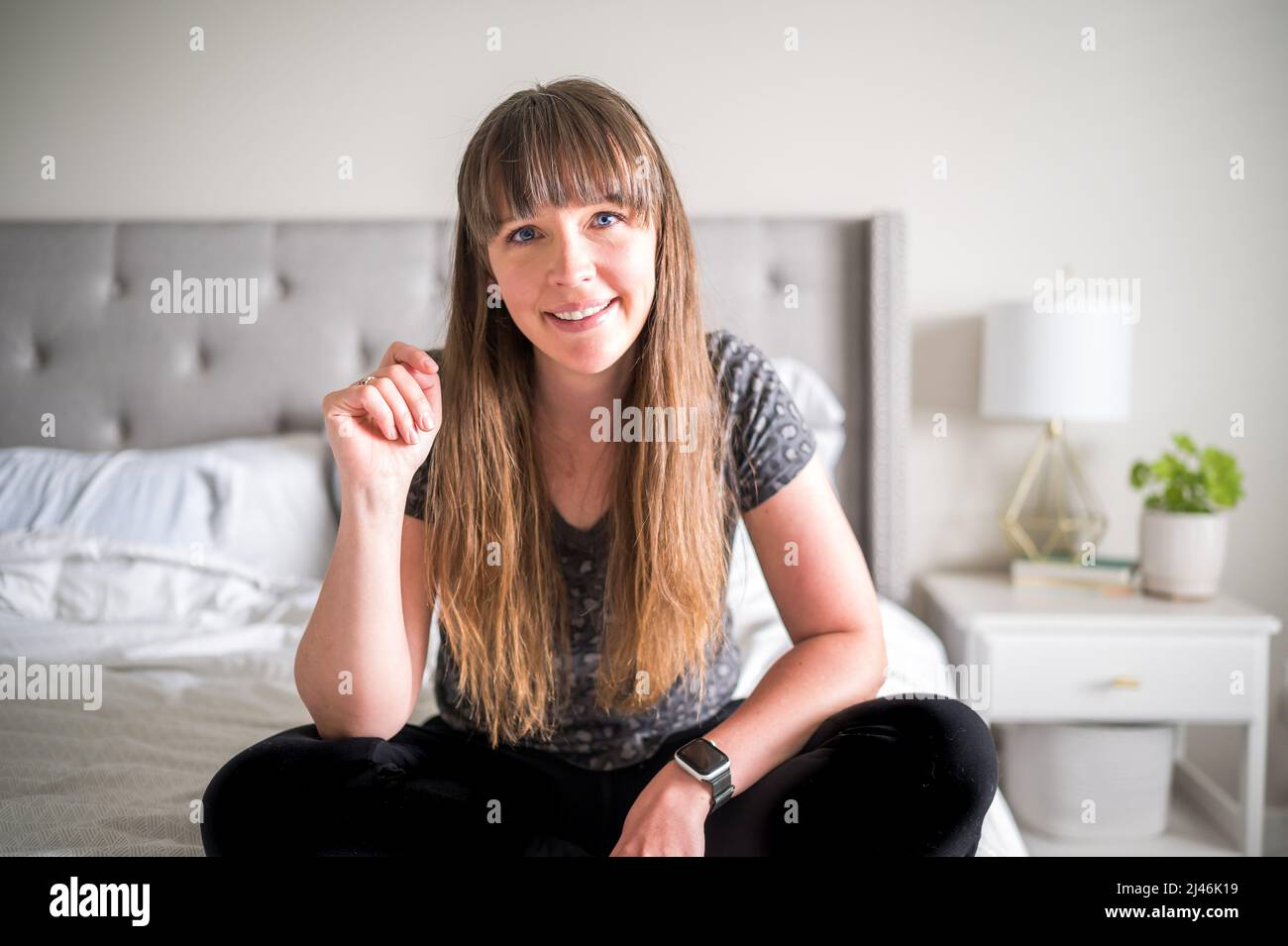 Caucasian woman with brown hair and bangs sitting on a bed Stock Photo