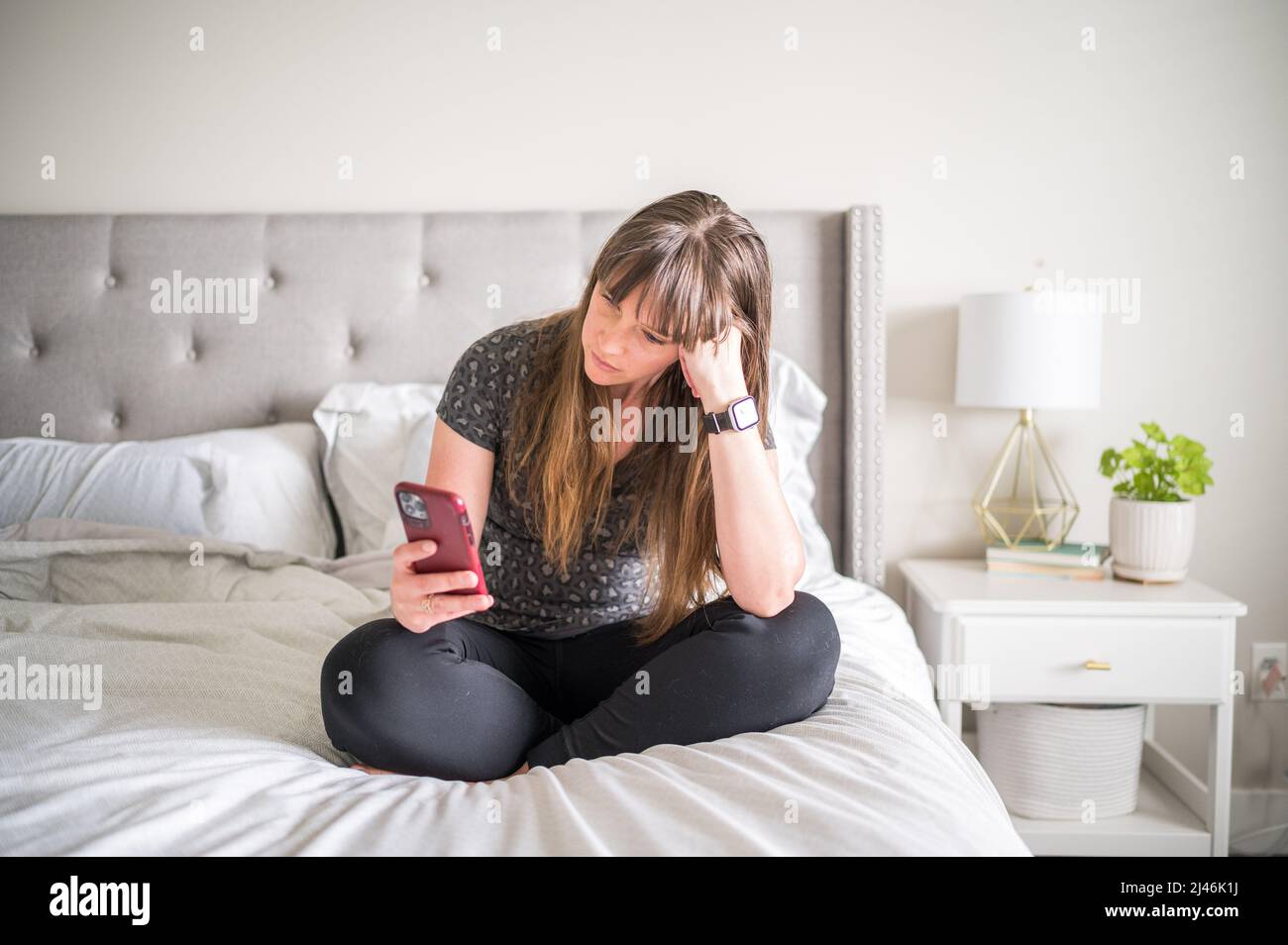 Woman sitting on bed while scrolling on her phone Stock Photo