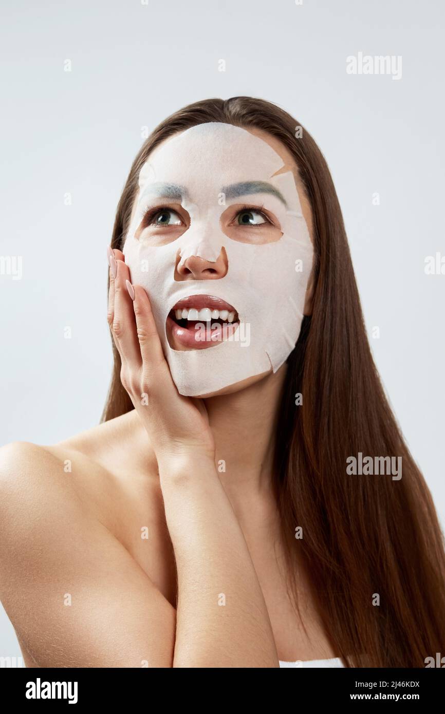 Beauty Facial Mask . Beautiful Young Woman with a cloth moisturizing mask on face .Skin care .Girl beauty model  touches her face.  Facial treatment Stock Photo