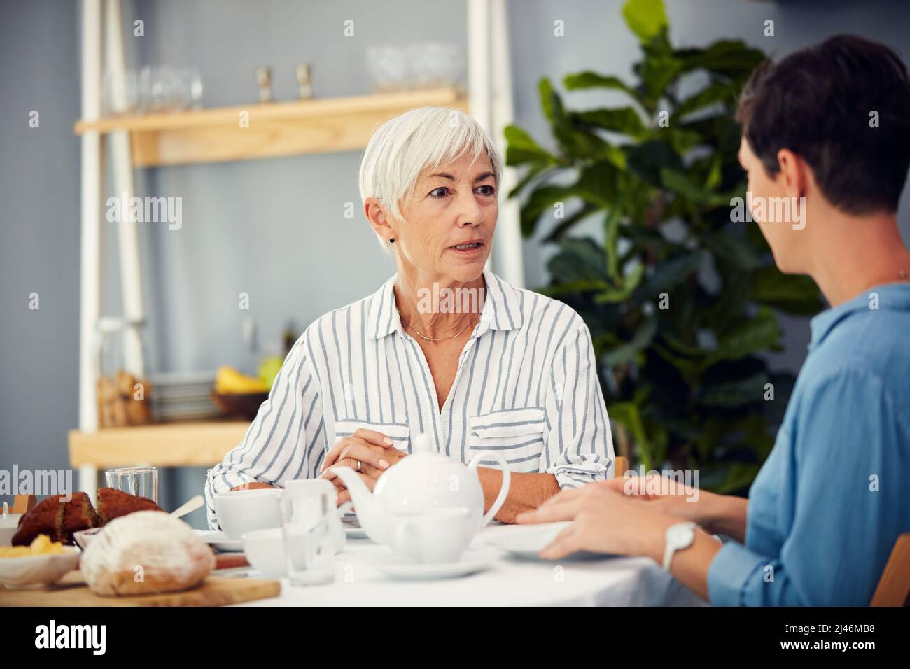 Her story-telling nature never changed. Cropped shot of an affectionate senior woman having tea with her daughter on a dining table at home. Stock Photo