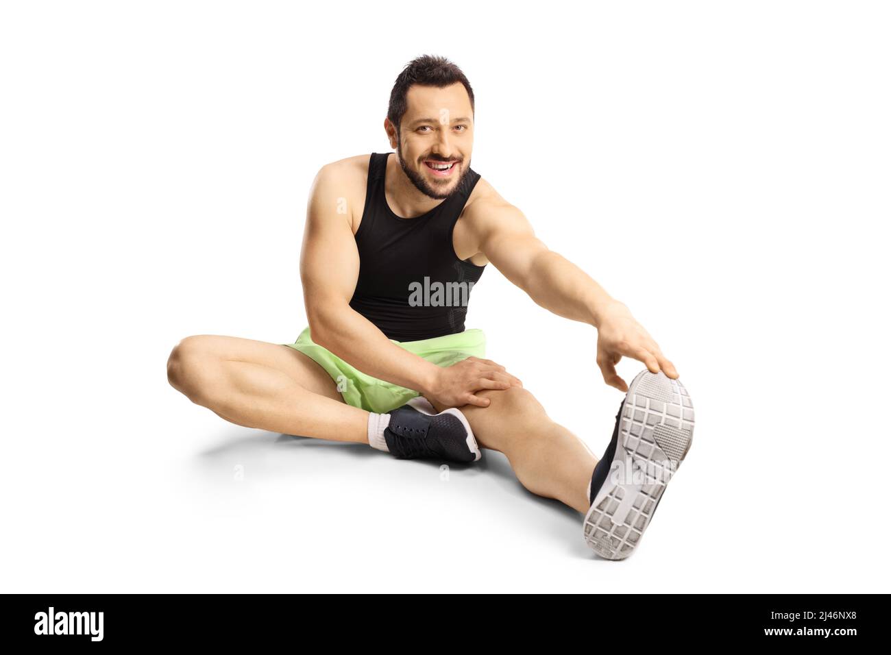 Young man in sportswear sitting on floor and stretching isolated on white background Stock Photo