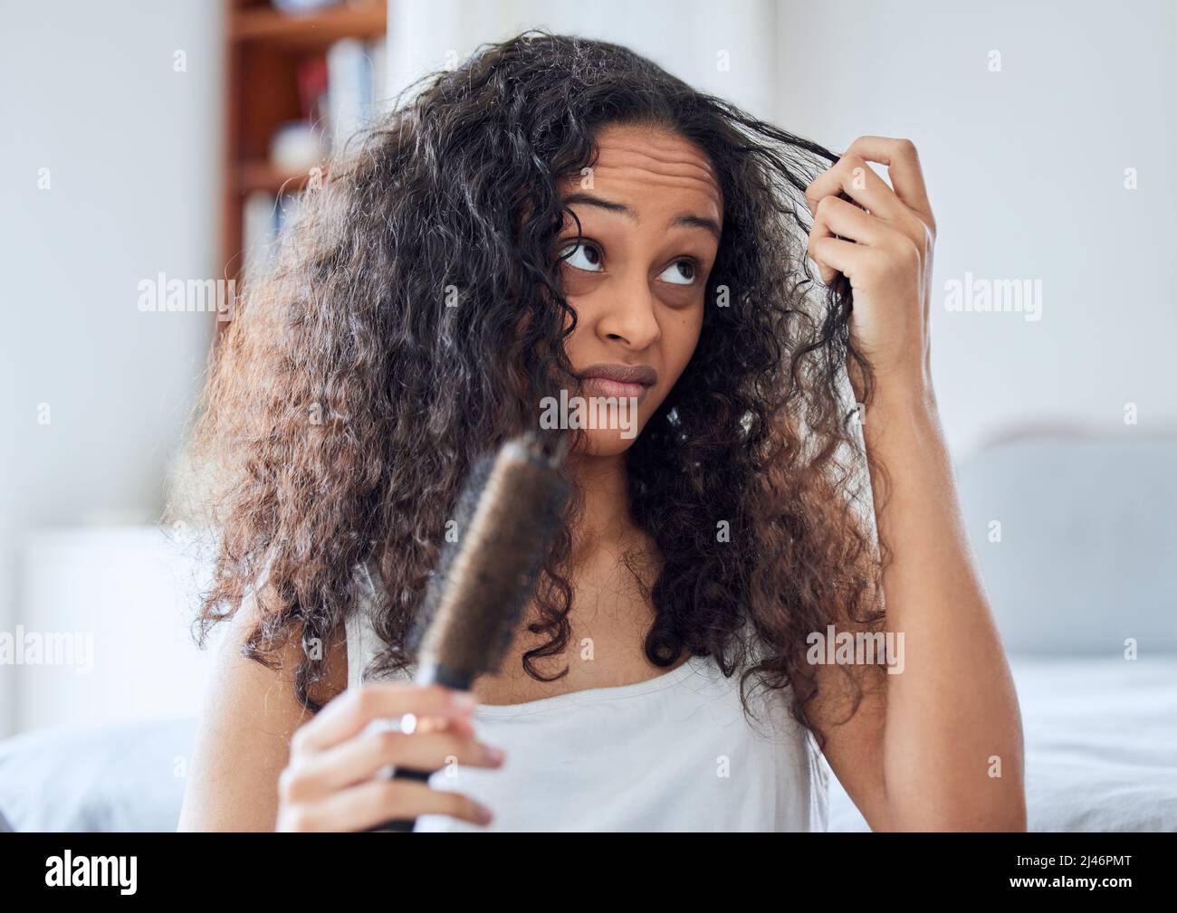 Urgh, what am I going to do with you. Shot of an attractive young woman standing alone at home and brushing her curly hair in the morning. Stock Photo