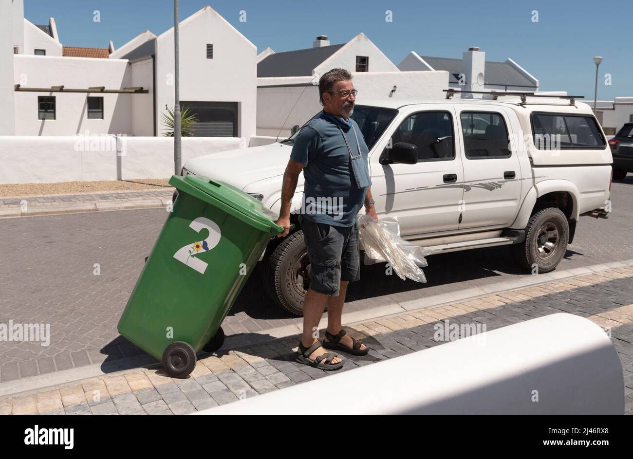West Coast, South Africa. 2022.  Resident moving an empty green recycling bin from the highway onto his property. Stock Photo