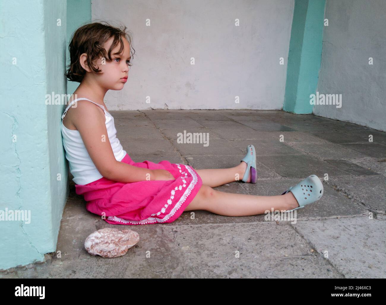 Cute angry girl is sitting on the floor near big stone. Concept of children behavior problem. Stock Photo