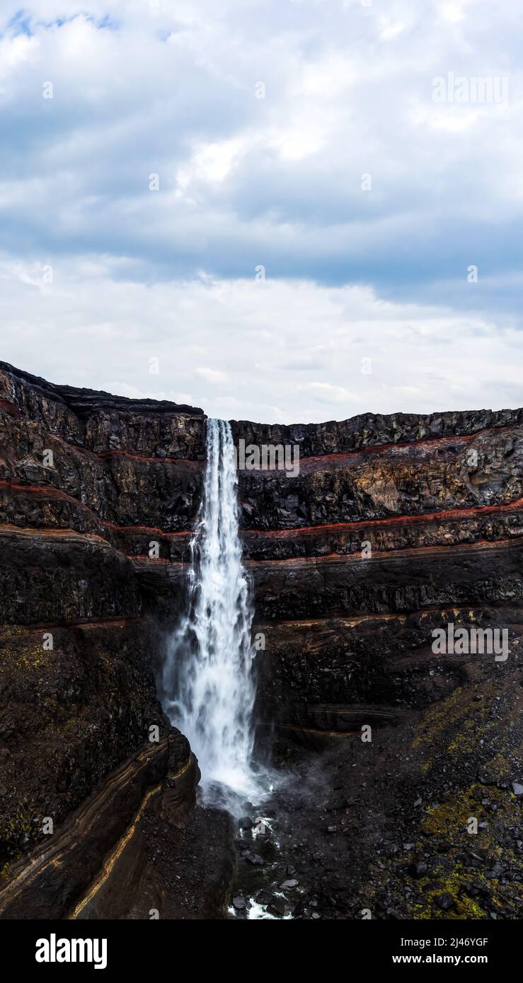 Hengifoss waterfall with deep red layers under cloudy sky Stock Photo