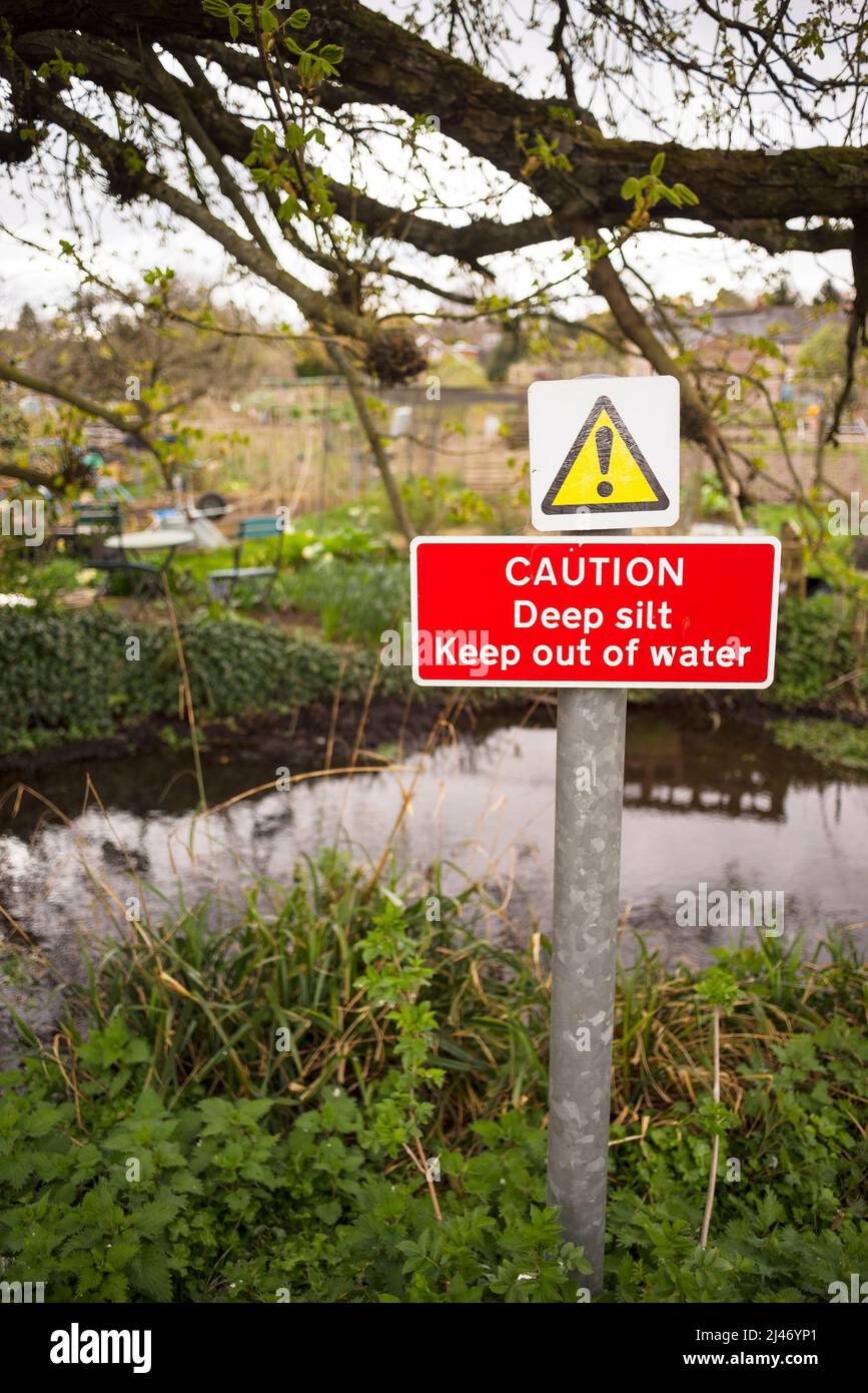 A sign warning of deep silt on the bank of a channel of the River Itchen near St Cross, Winchester, Hampshire Stock Photo
