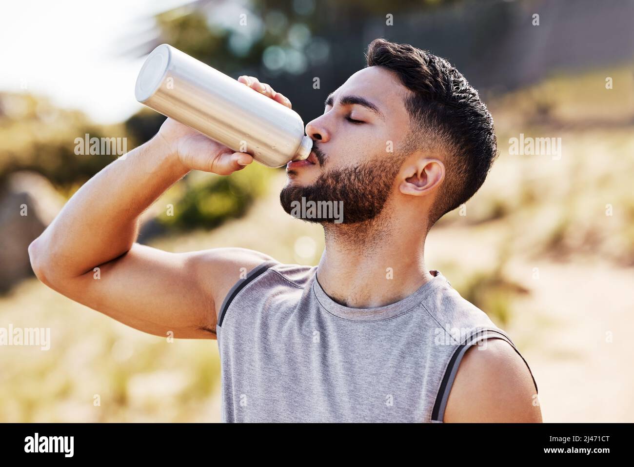 Staying hydrated is how I can keep going. Shot of a handsome young man standing alone outside and drinking water during his run. Stock Photo