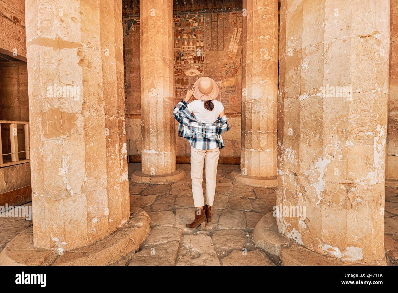 Happy woman traveler explores the ruins of the ancient egyptian Hatshepsut temple in the heritage city of Luxor. Columns with painted hieroglyph and c Stock Photo