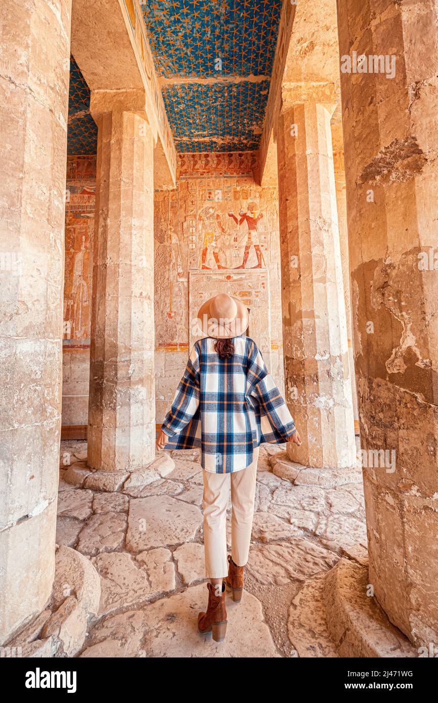 Happy woman traveler explores the ruins of the ancient egyptian Hatshepsut temple in the heritage city of Luxor. Columns with painted hieroglyph and c Stock Photo