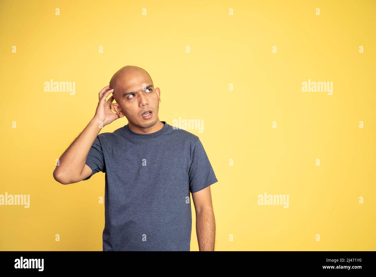 asian bald man daydreaming while glancing up holding head Stock Photo