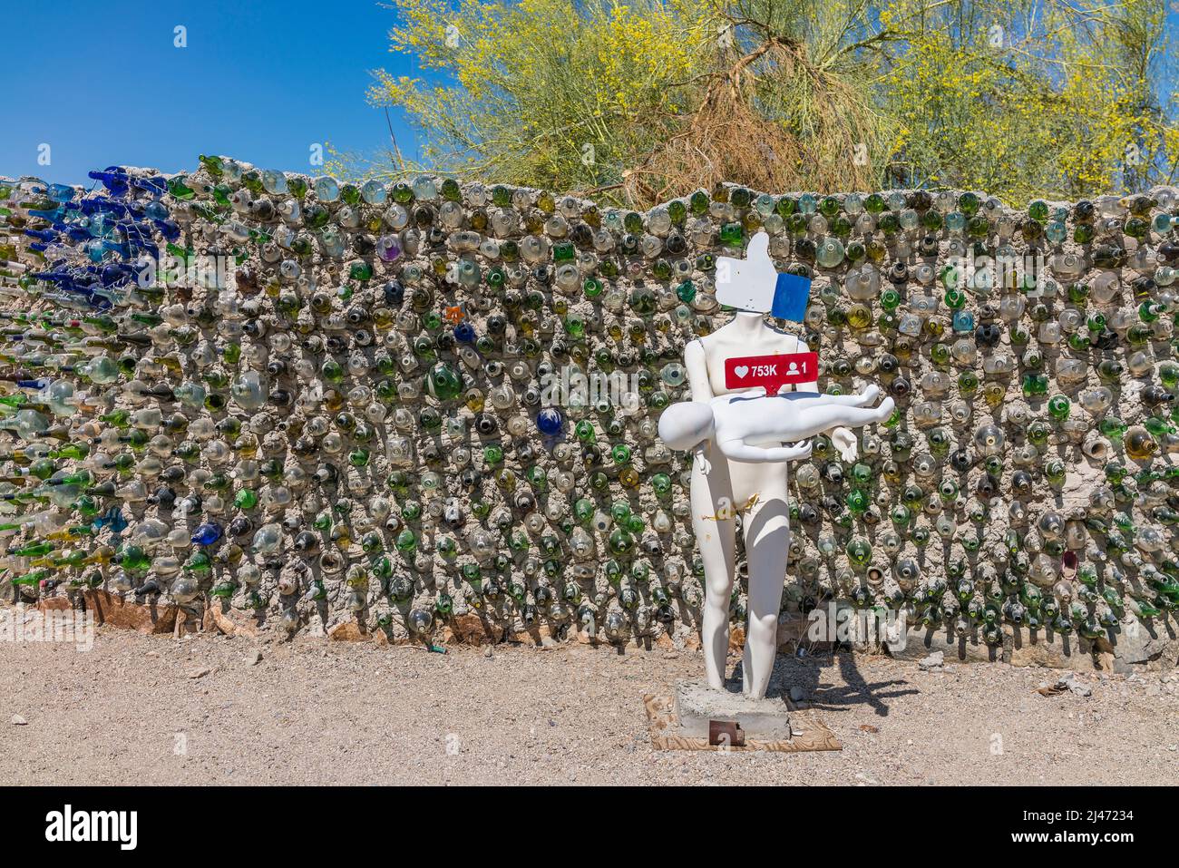 White figure sculpture holding baby in front of glass wall made of glass bottles in concrete in the settlement of East Jesus in Southern California. Stock Photo