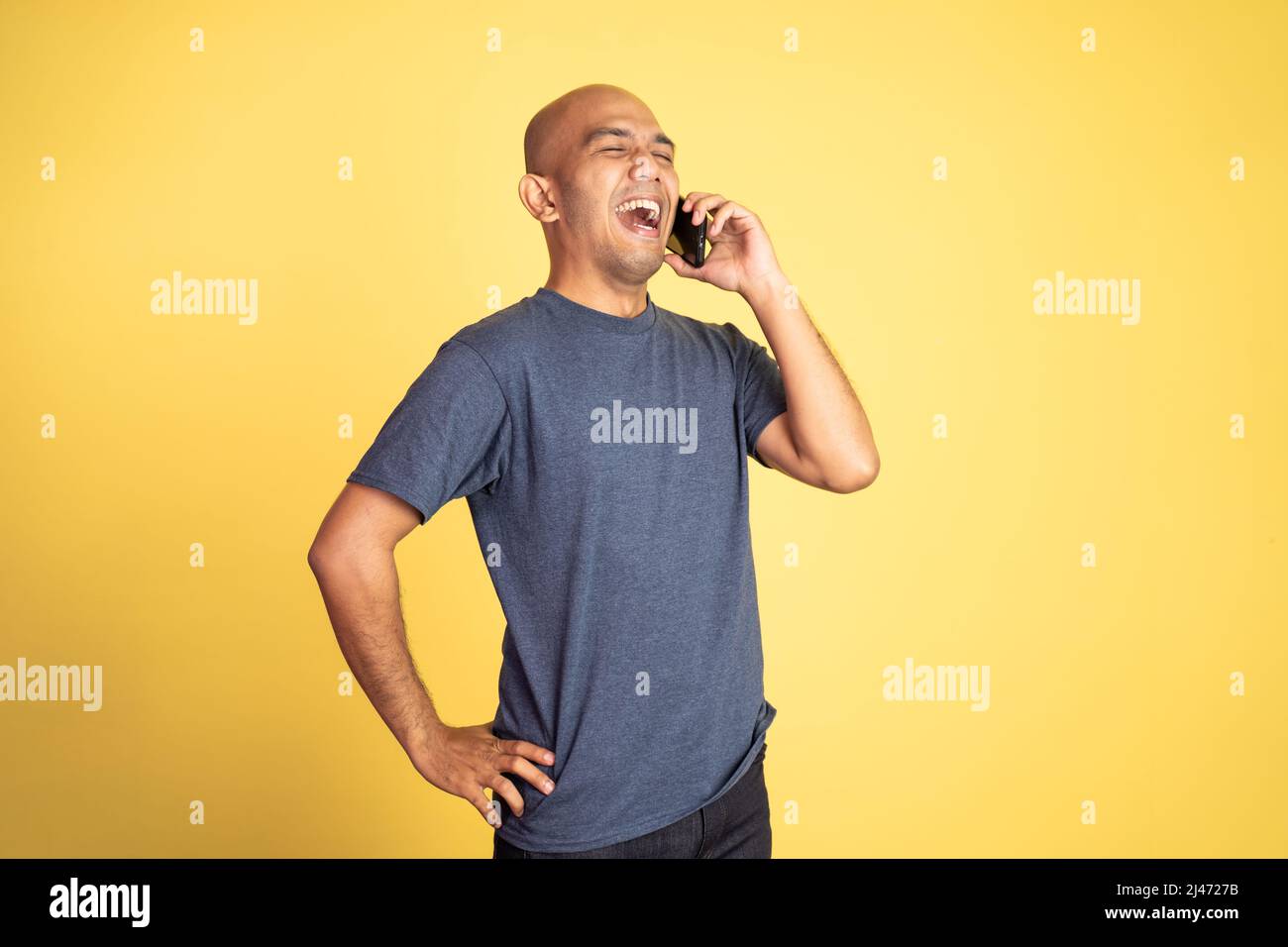 bald young man laughing while making phone call Stock Photo