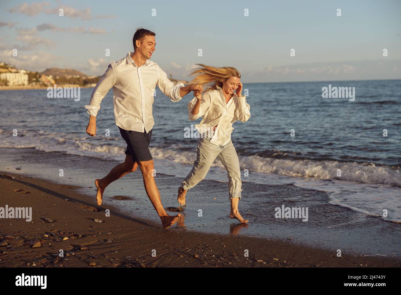 Beautiful couple running on the beach holding hands Stock Photo - Alamy