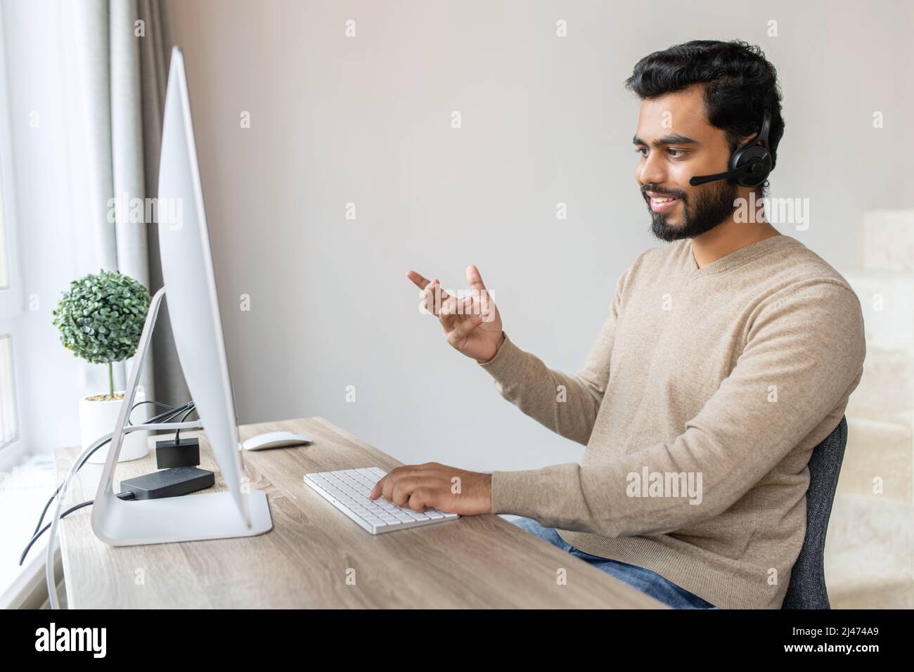 Portrait of cheerful Indian guy in wireless headset using laptop ...