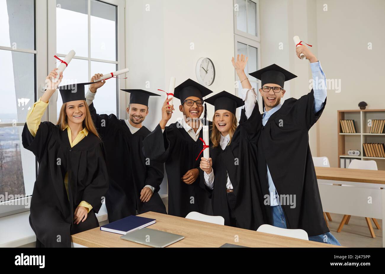 Group of happy joyful diverse university graduates in caps and gowns holding up diplomas Stock Photo