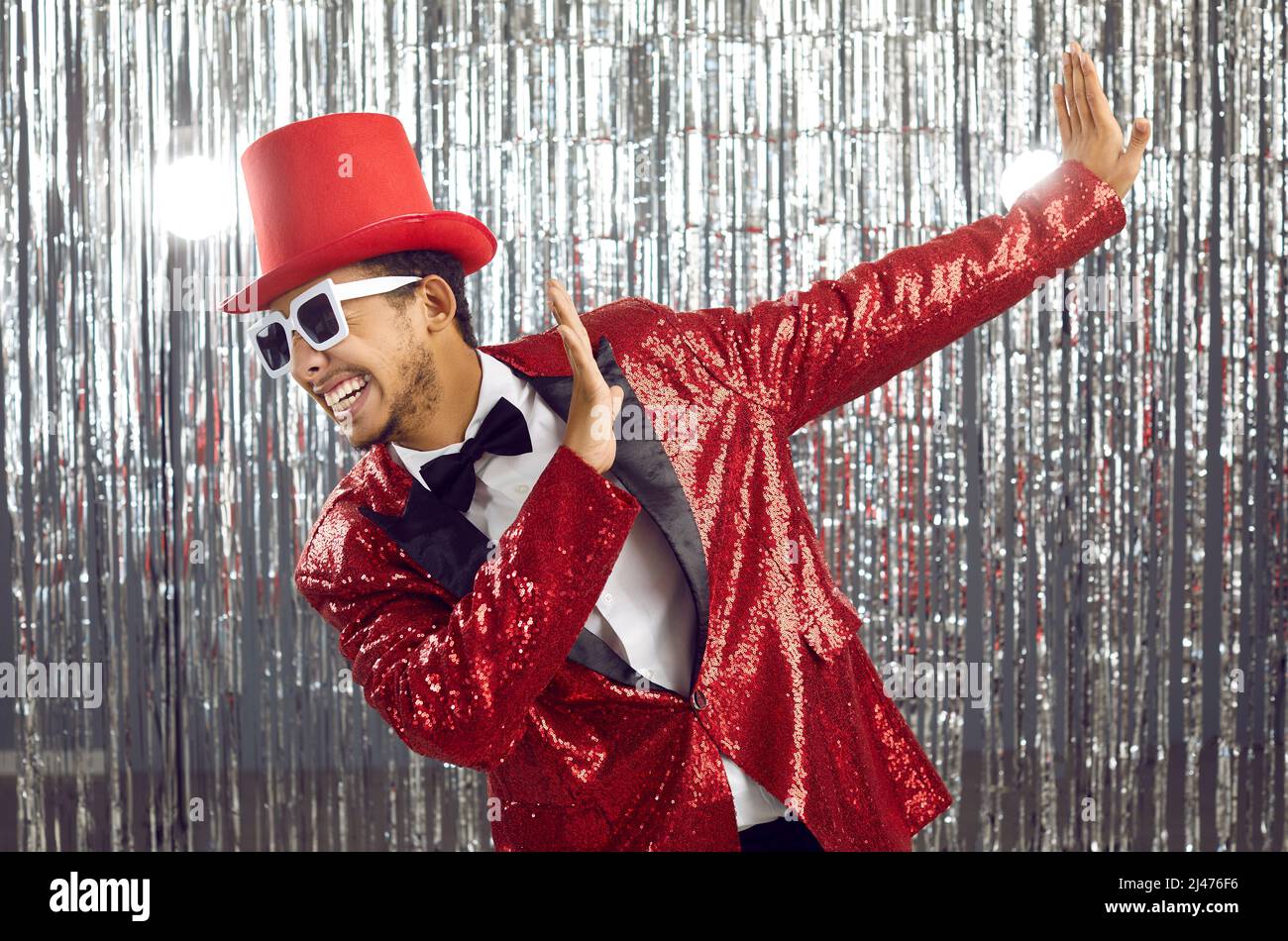 Funny young black guy in a sequin jacket, top hat and sunglasses dancing at a party Stock Photo