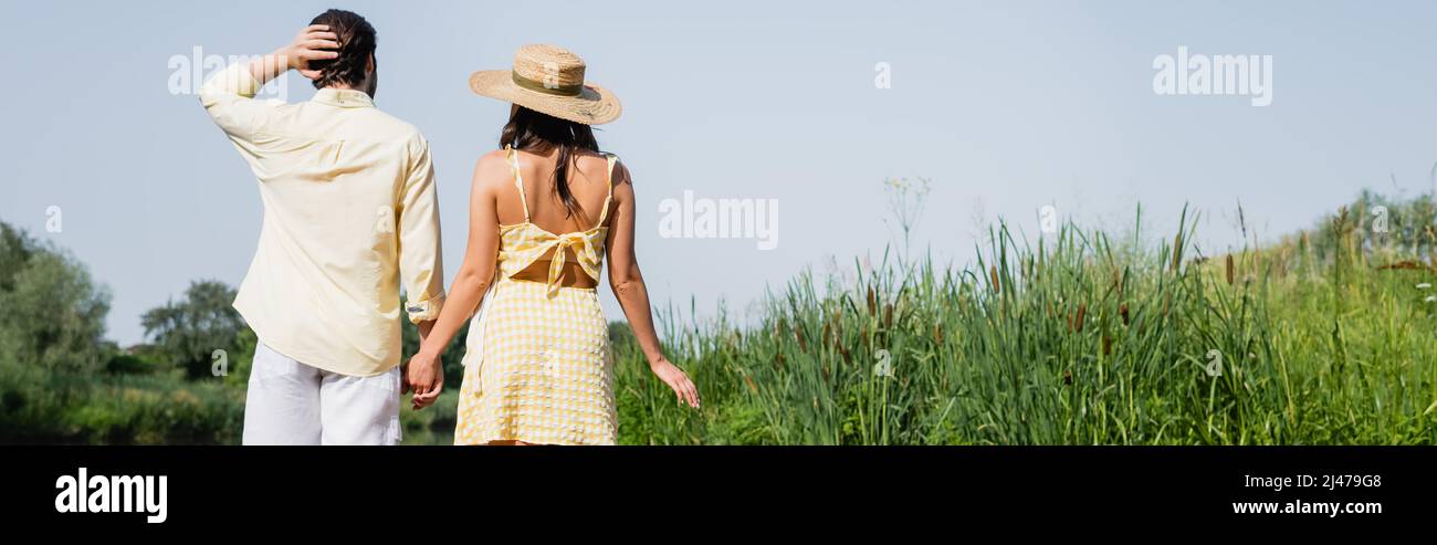 back view of young couple in summer clothes holding hands and standing ...