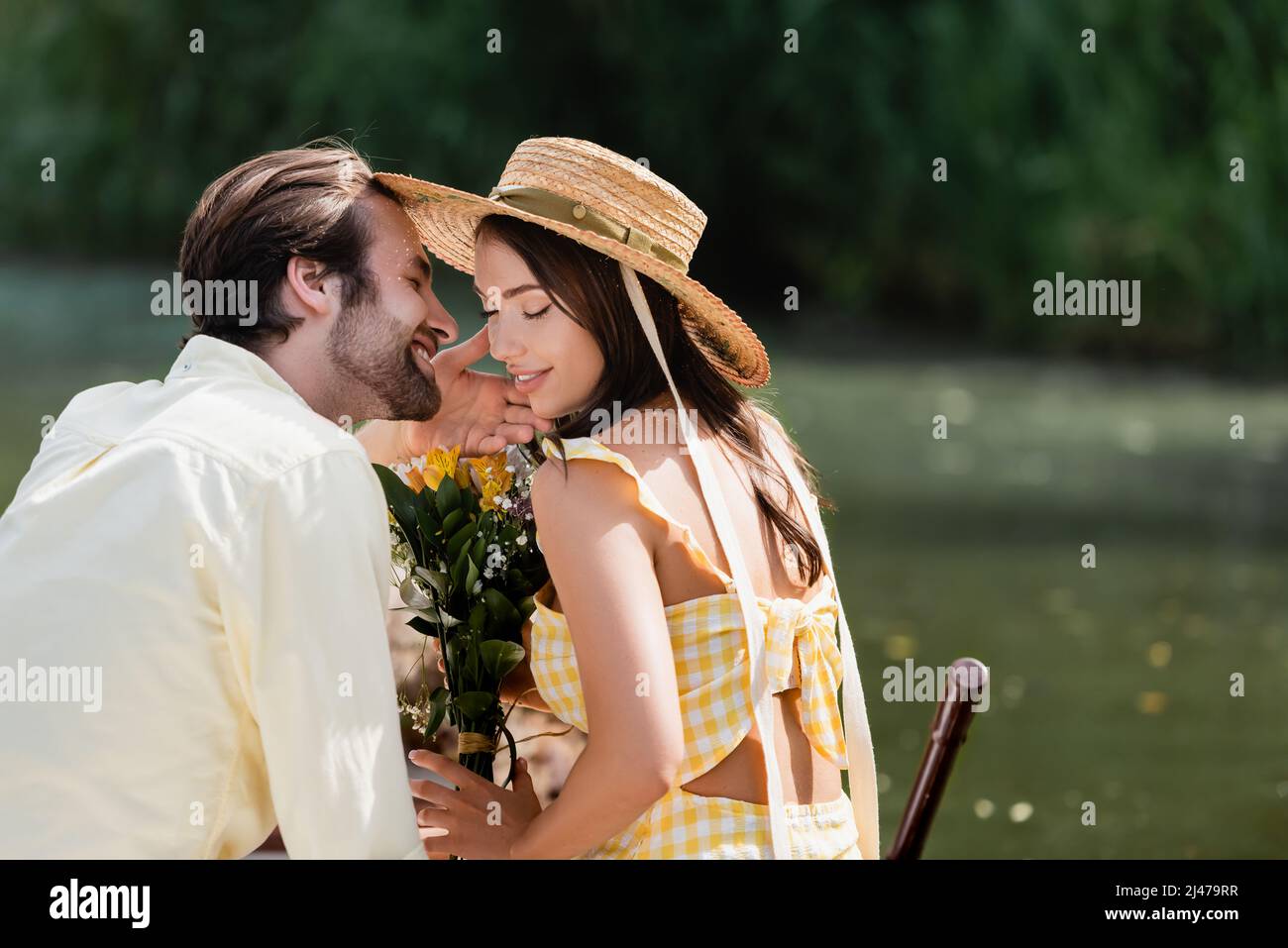 happy young woman in straw hat holding bouquet of flowers near romantic ...