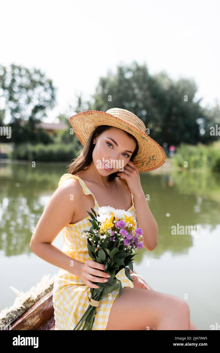 pretty young woman in straw hat and dress holding flowers while sitting ...