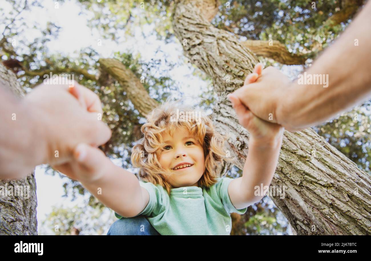 Happy boy climbing a tree during summer time. Fathers hand. Stock Photo