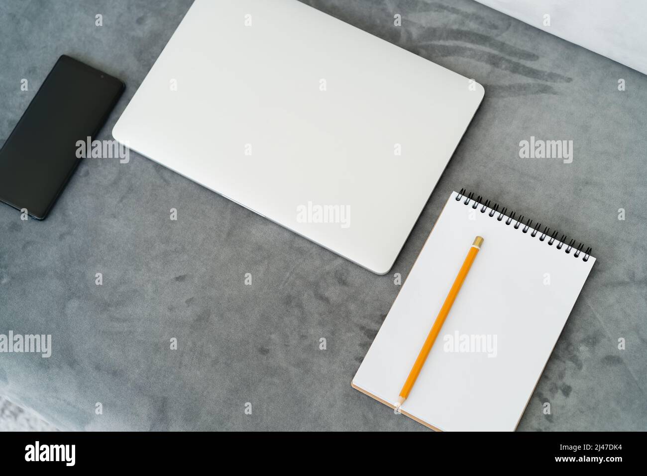 top view of closed laptop, empty notebook with pencil and smartphone with blank screen on grey surface Stock Photo