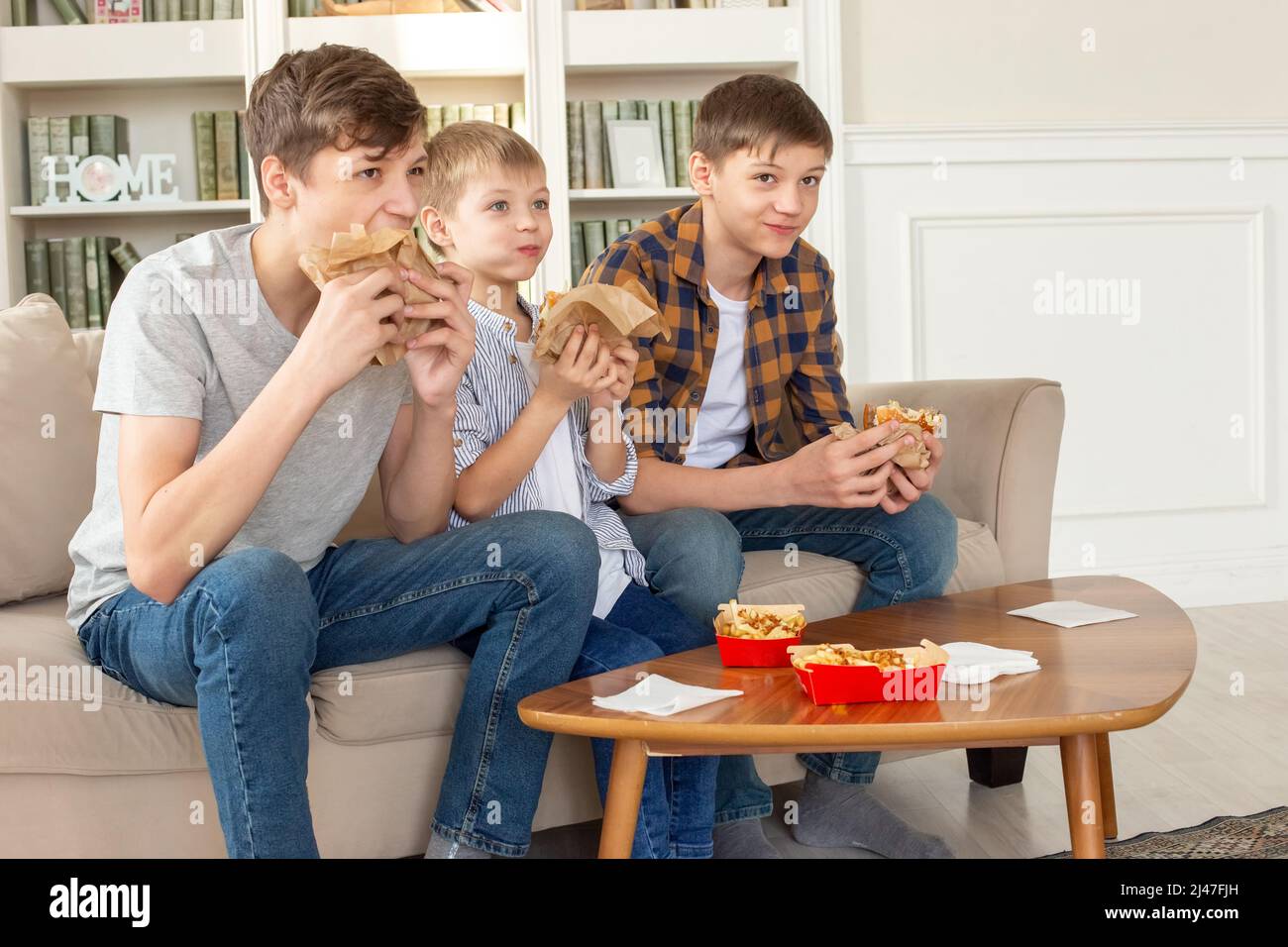 A cute three teenage boys, eating fast food in living room, watch tv Stock Photo