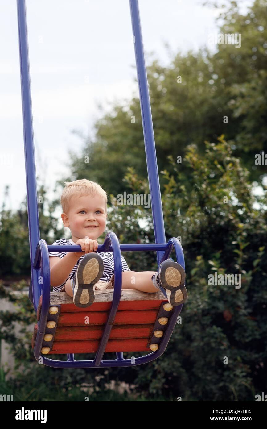 Happy, smiling child is swinging on a swings in a park at summer Stock Photo