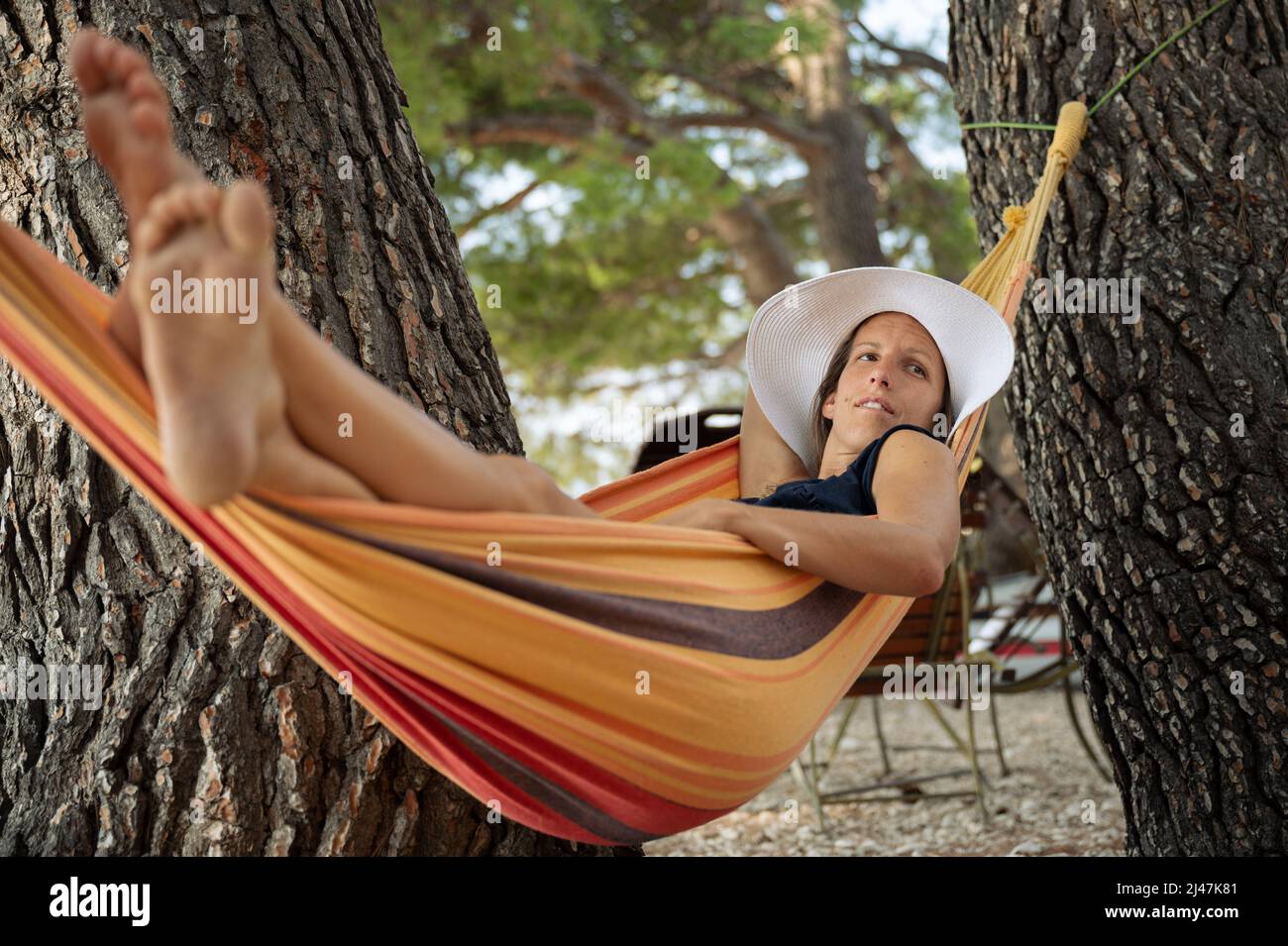 Sun tanned young woman lying in a hammock between pine trees in a summer holiday resort. Stock Photo
