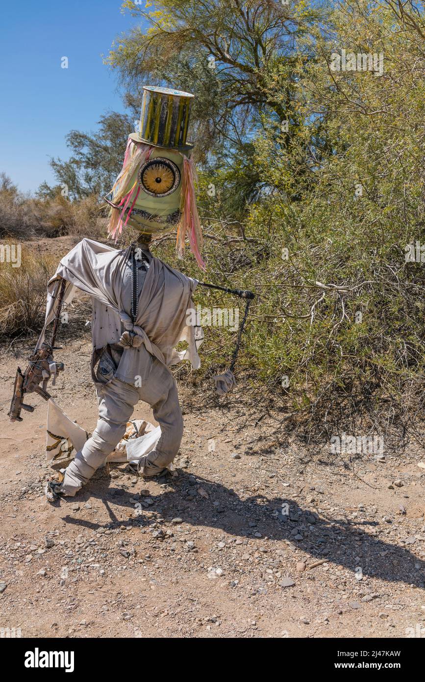 Freakish creature sculpture with one large, orange eye, multicolored hair, a huge top hat, and a homemade gun, attempting to stand in the desert in th Stock Photo