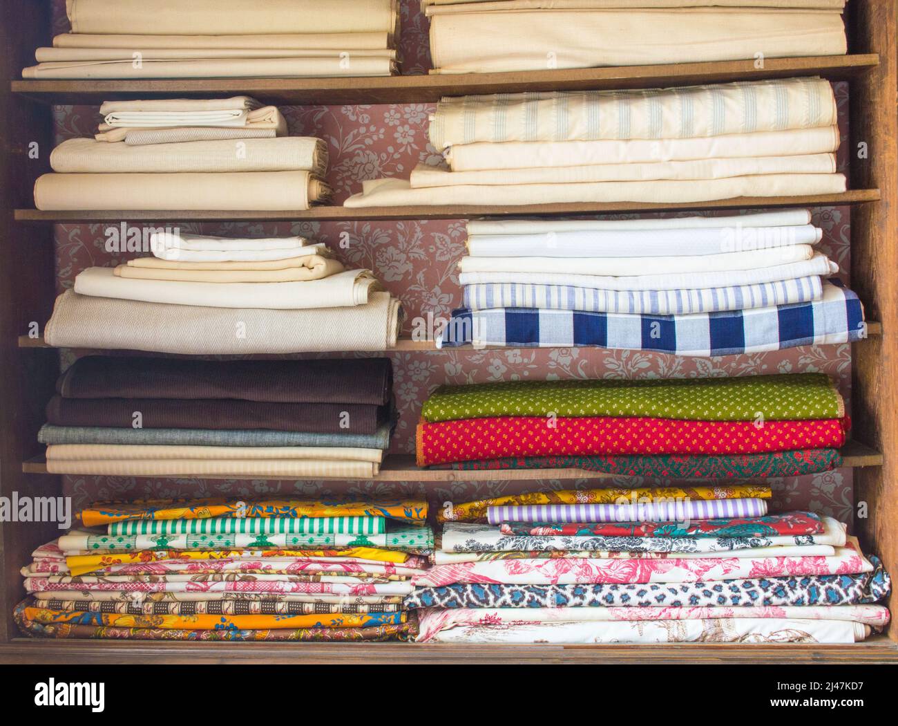 rustic wooden shelves filled with stacks of colorful colonial fabrics Stock Photo