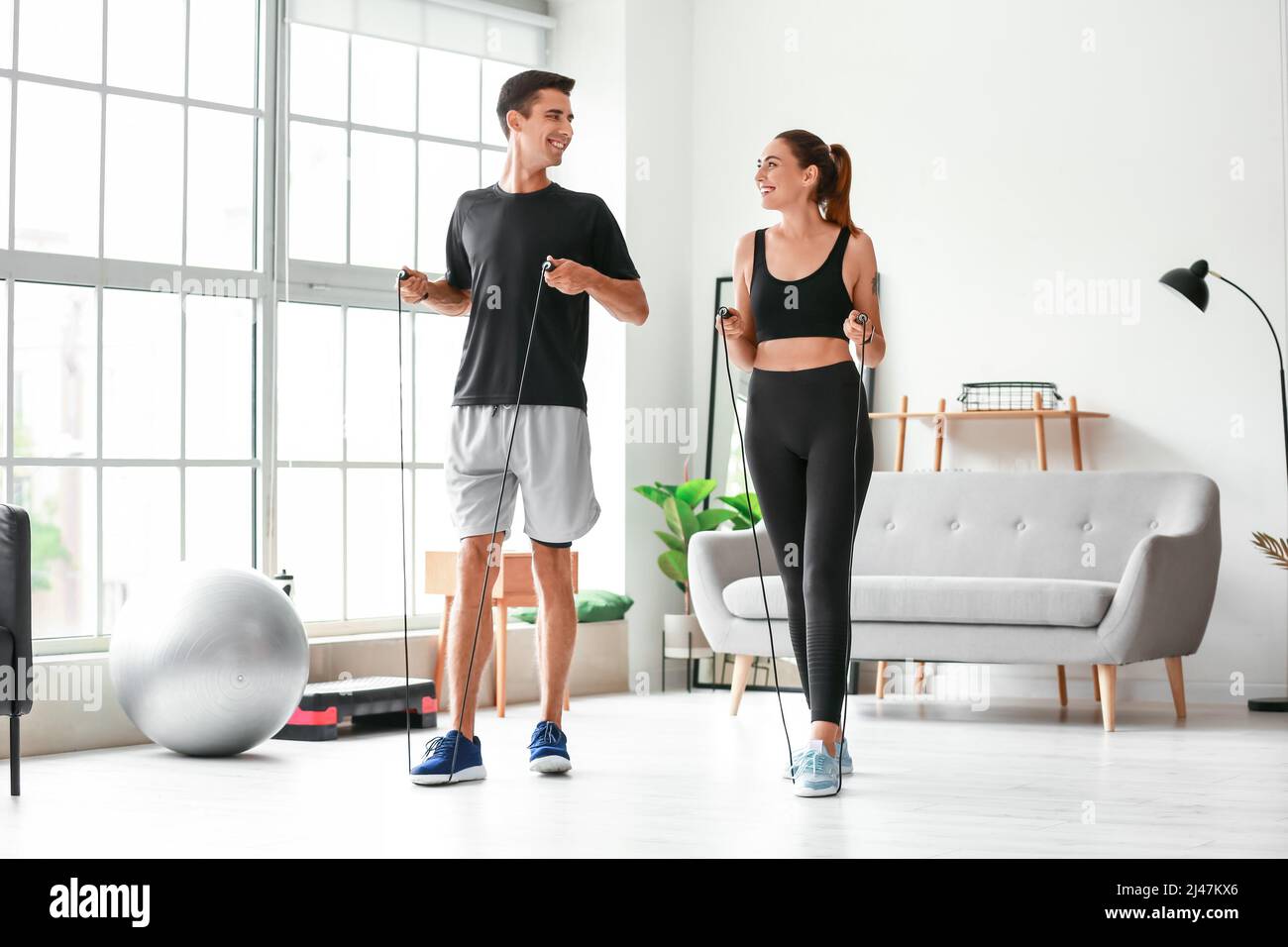 Sporty young couple jumping rope at home Stock Photo - Alamy