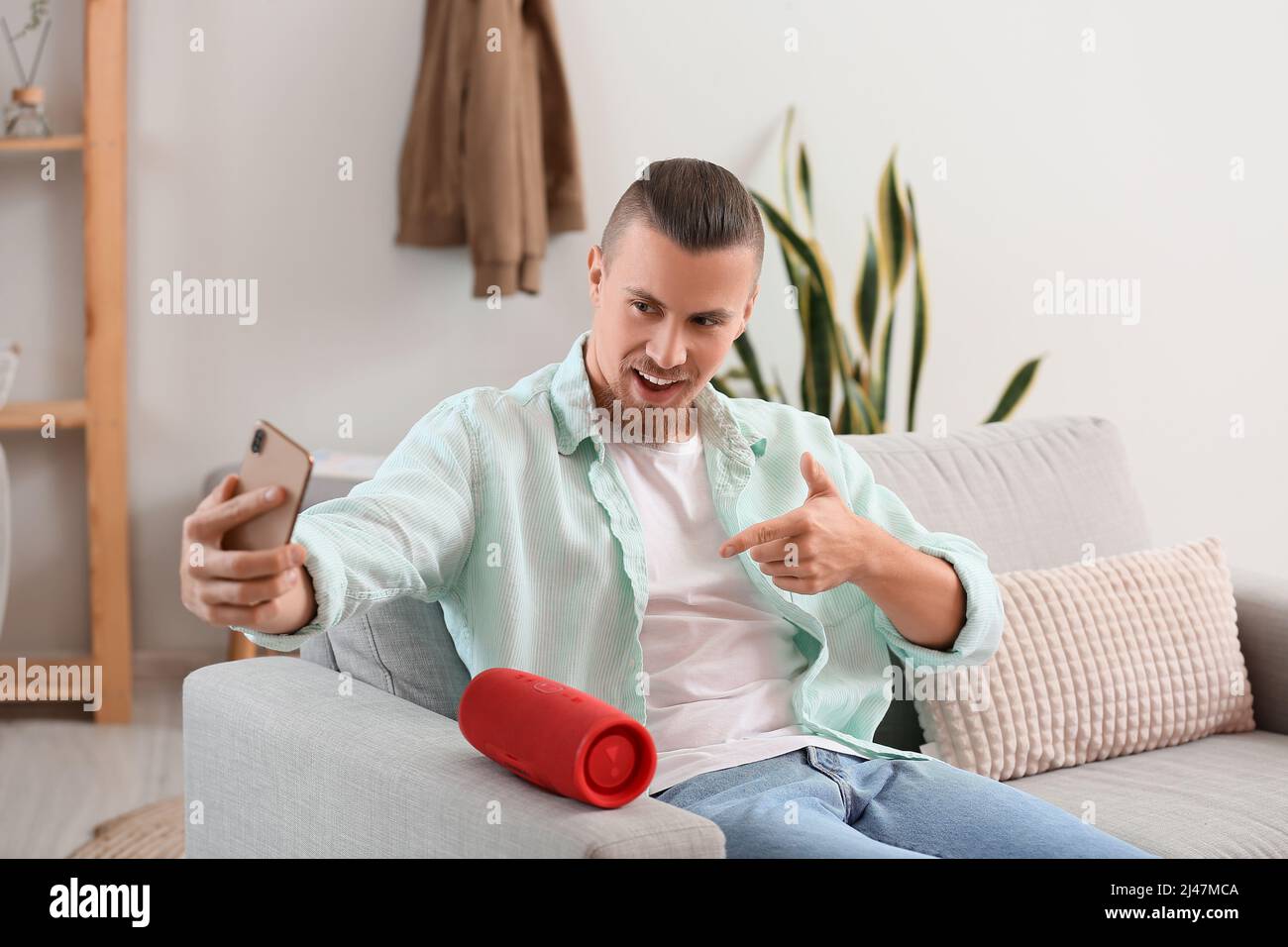 Man taking selfie with modern wireless portable speaker on sofa in