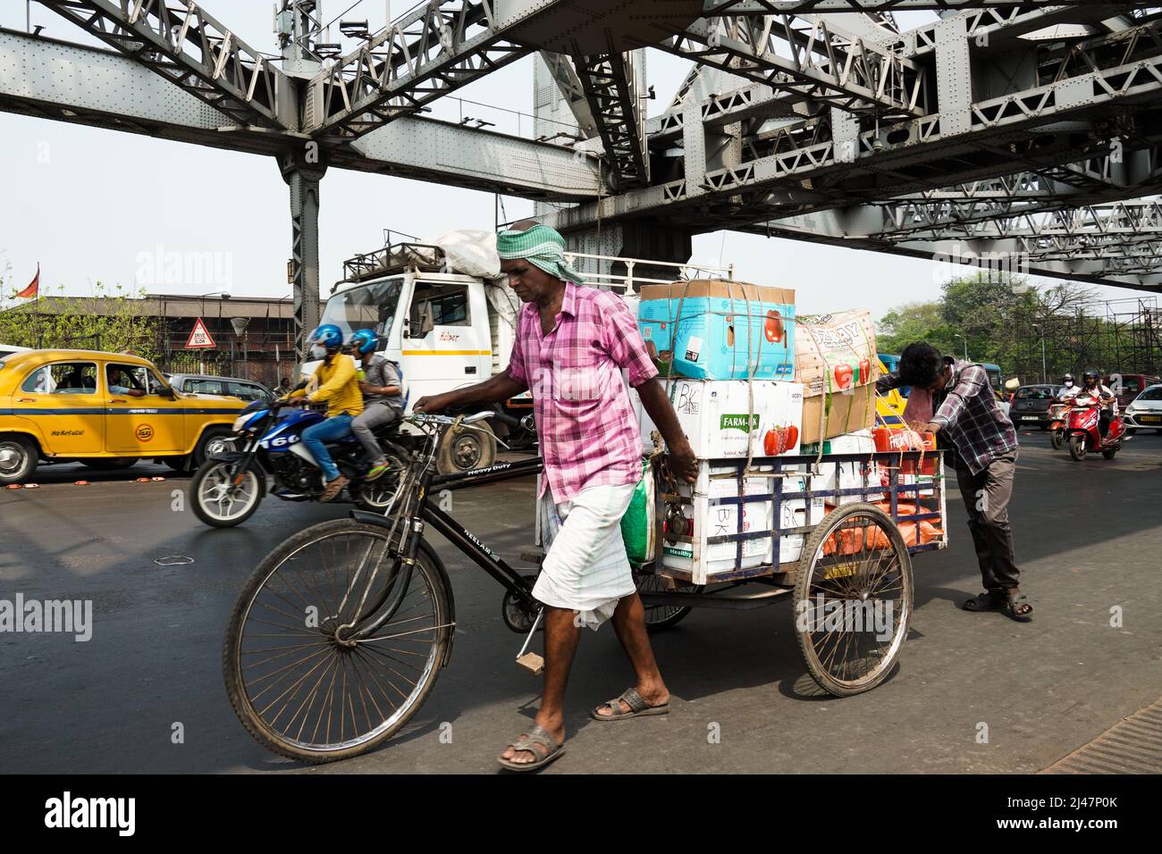 India, West Bengal, Kolkata, Men push a cart loaded with goods across Howrah Bridge Stock Photo