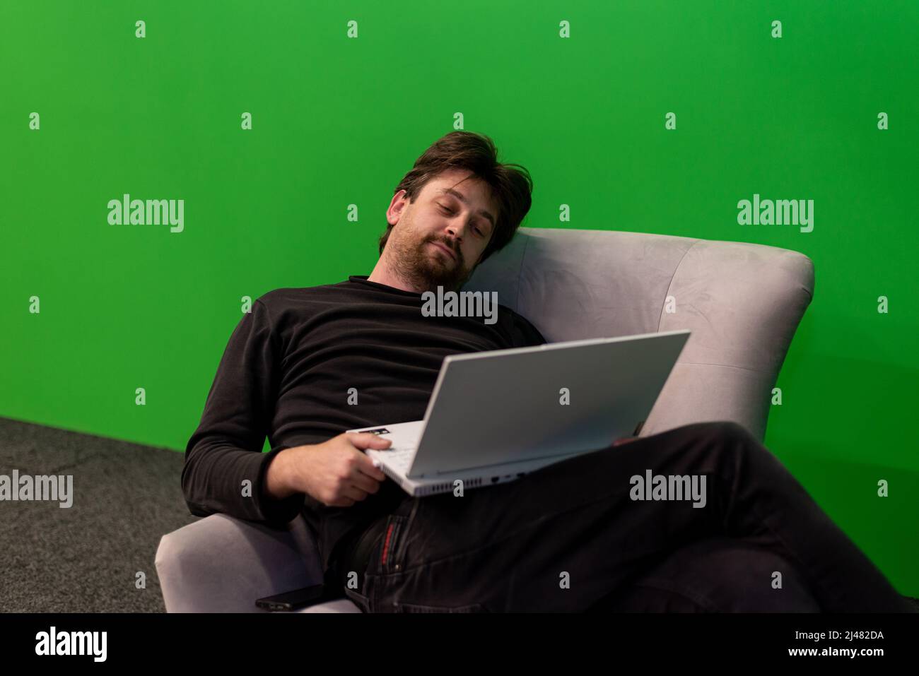 Tired man reading emails on laptop on green screen Stock Photo