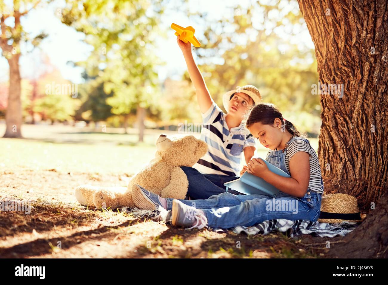 Enjoying their own little adventures at the park. Shot of two little siblings having fun while sitting on a blanket at the park. Stock Photo