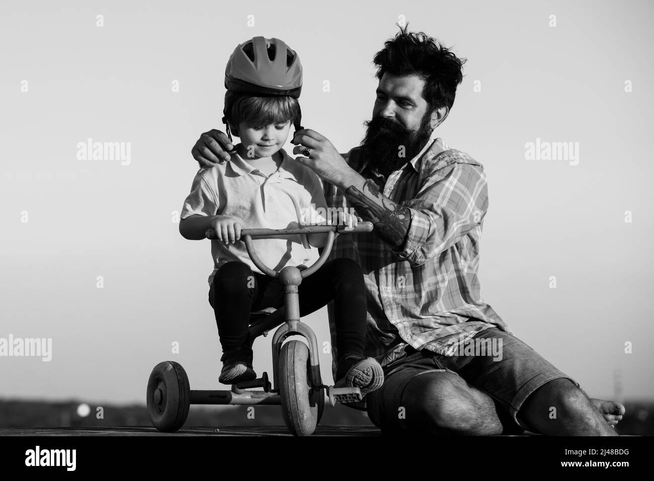 Help kid explore world. Happy loving family Father and son. Little boy wearing helmet while learning to ride cycle with his daddy. Stock Photo