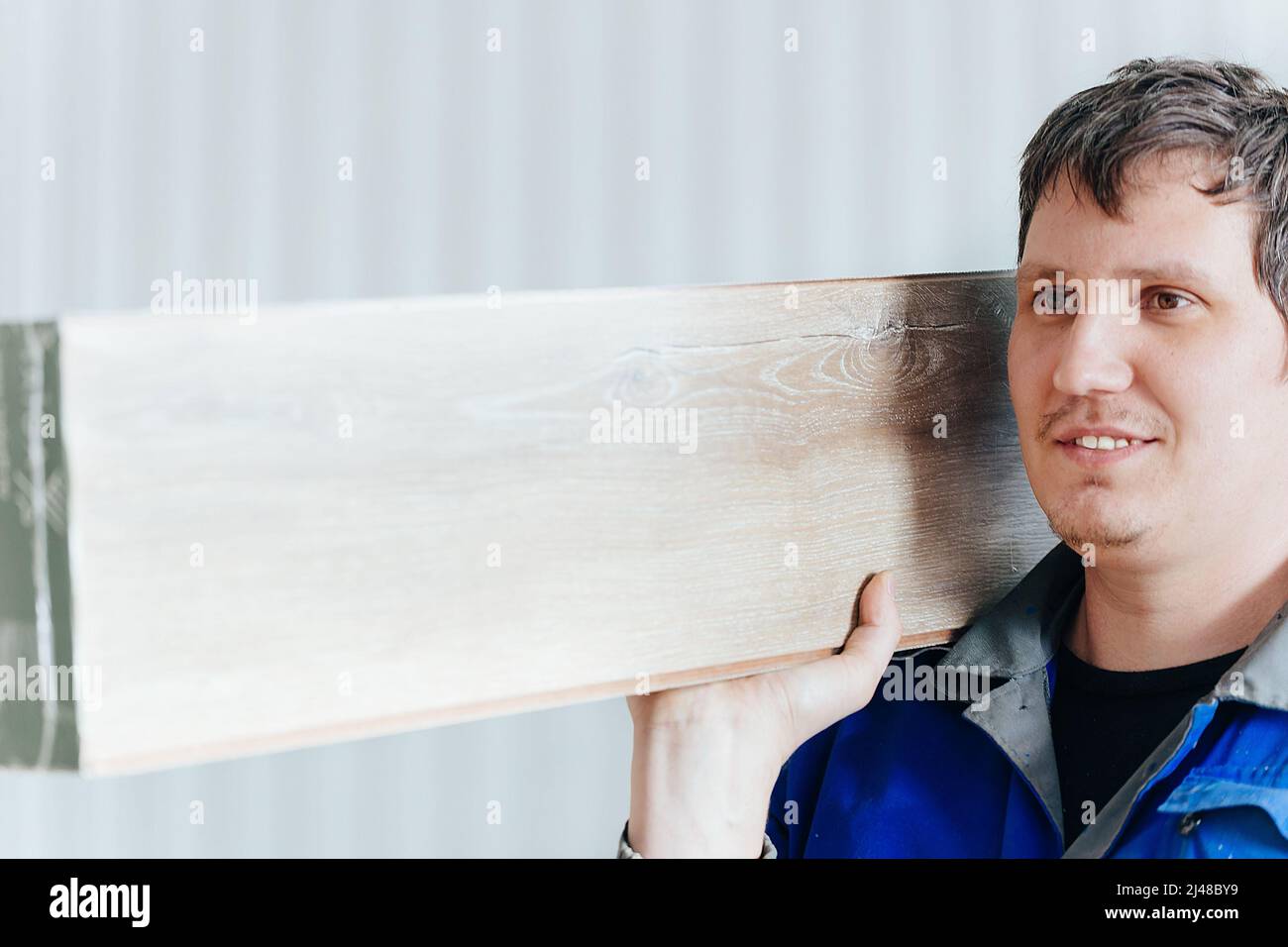 Young man of Caucasian appearance holds package of laminate on his shoulder. Delivery and installation of floor coverings. Implementation of parquet board. Stock Photo