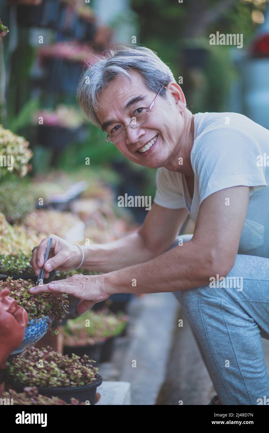 asian man toothy smiling with happiness taking care of houseplant at home garden Stock Photo