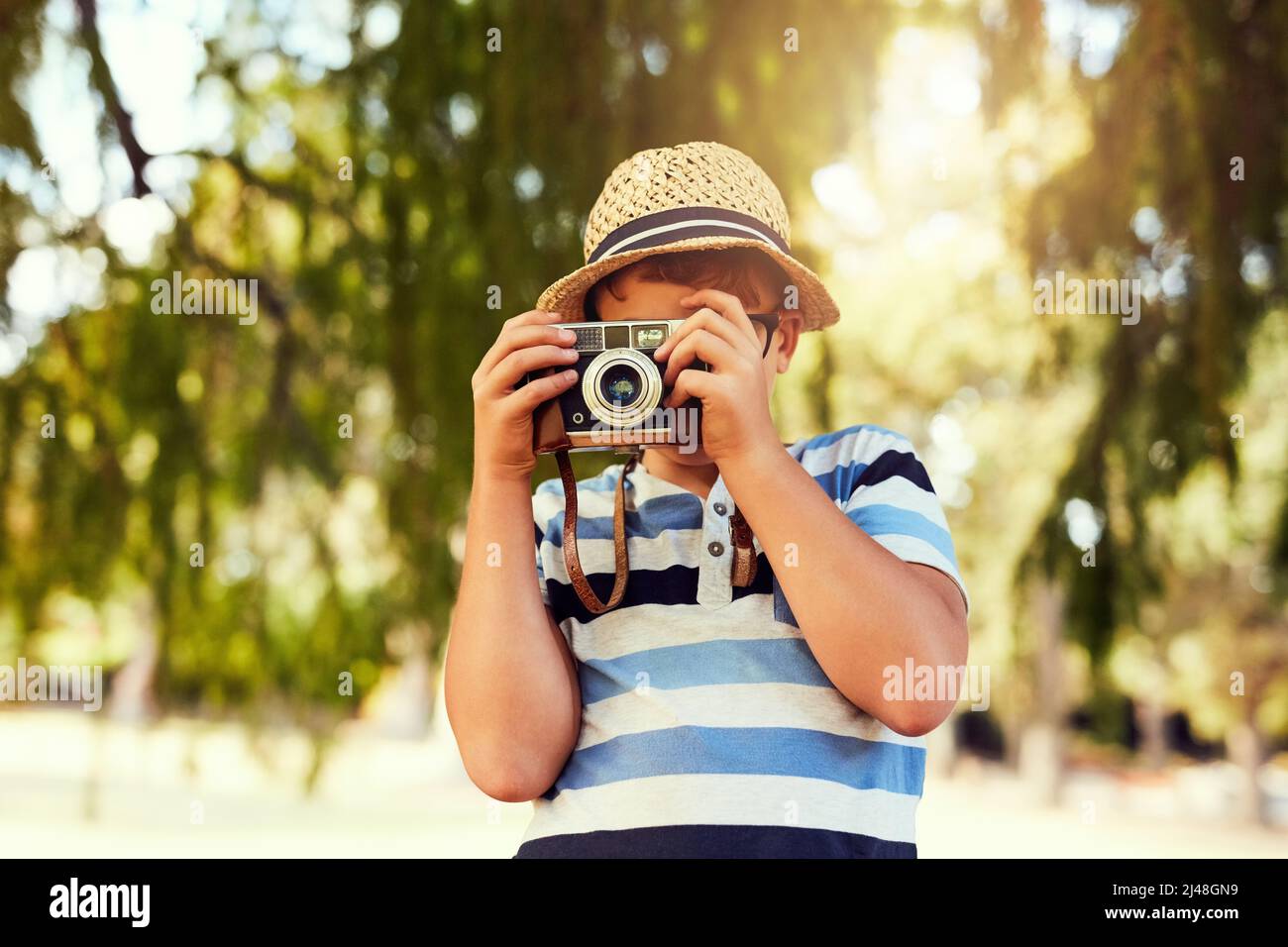 Seeing the world in a new light. Shot of a little boy taking a photo with a vintage camera at the park. Stock Photo