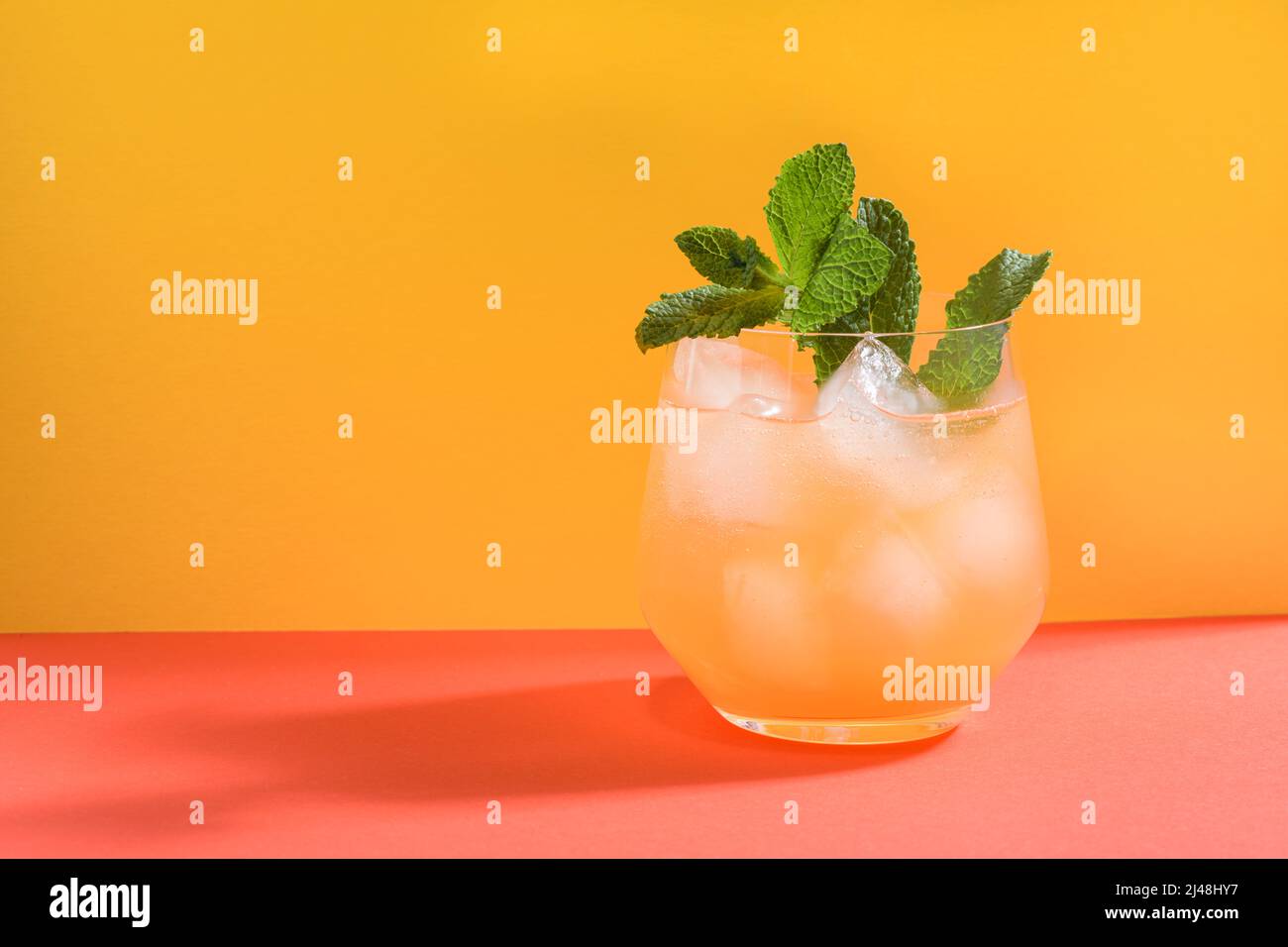 Cold drink with bubbles and ice cubes and mint leaves on top against an orange and red background Stock Photo